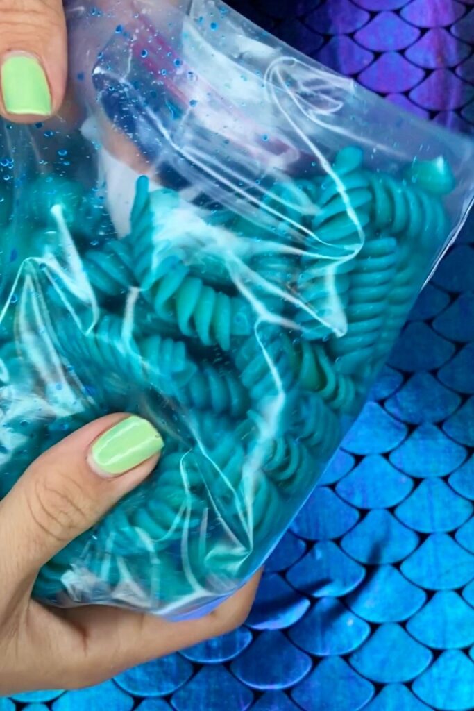 Blue food coloring is applied to pasta in a plastic bag to make mermaid macaroni and cheese