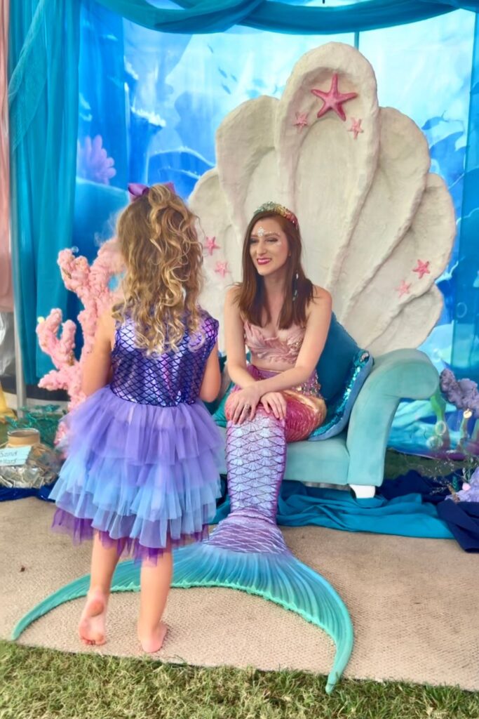 Little girl in a mermaid costume meets a mermaid in her clam throne